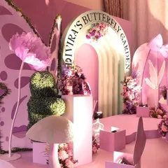 A wider view of the luxury butterfly garden party, showcasing oversized paper flowers, topiary elements, and a multi-level stage setup that adds depth and grandeur.