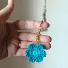 A close up of the turquoise floral keychain. The gold-tone hardware adds a touch of elegance to the handmade crochet flower.