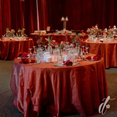 The tables were set with deep orange linens, hammered metal charger plates, and rich red napkins. Centerpieces of red flowers in clear glass vases, surrounded by candles, created an intimate and warm dining setting.