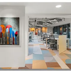 A vibrant piece of abstract art adds a splash of color to this modern office hallway. The view extends into the open-plan workspace, showcasing the dynamic and creative environment.