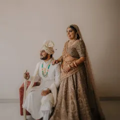 A regal, full-length portrait. The groom is seated holding a ceremonial sword, while the bride stands by his side, creating a powerful and traditional image.