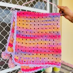 A beautiful multi-colored striped blanket personalized with the name "Adhira." The soft lavender border and matching pom-poms add a playful touch. This is a perfect example of a custom name blanket for a newborn.