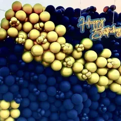 A bold and stylish balloon wall for a birthday celebration. The combination of matte navy blue and metallic gold balloons, paired with a 'Happy Birthday' neon sign, creates a dramatic and modern backdrop.