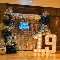 This 19th birthday had a sleek and modern vibe with a silver and black color scheme. The setup includes a full shimmer wall, marquee light-up numbers, and balloon columns with clear confetti balloons for extra texture.