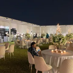 Simplicity is the ultimate sophistication. This minimalist outdoor reception features clean white tables, quilted cream chairs, and elegant floral centerpieces with candles, creating a serene and classy atmosphere on the lawn.