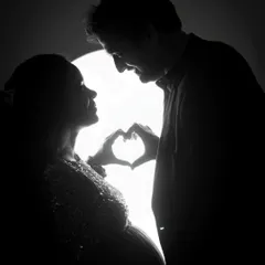 A beautiful silhouette of an expecting couple making a heart shape with their hands. This creative shot is a romantic and artistic way to celebrate their love and new beginning.