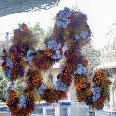 An abstract, free-floating floral sculpture named 'Azure Ochre'. The design mimics the texture and movement of volcanic lava, using a vibrant and unconventional color palette of blue, orange, and deep reds.