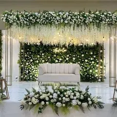 For a sophisticated engagement or reception, nothing beats a classic white and green theme. This stage features a lush green wall covered in white roses, with hanging wisteria flowers and a custom neon sign, creating an elegant and romantic setting.