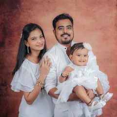 A classic family portrait against a warm, textured backdrop. Everyone is looking at the camera, making this a perfect photo for framing and sharing with loved ones. The simple white outfits keep the look clean and elegant.