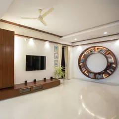 This modern living room features a stunning circular bookshelf that serves as a unique piece of wall art. The clean lines of the TV unit, white marble floors, and ample natural light create a space that feels open, bright, and sophisticated.