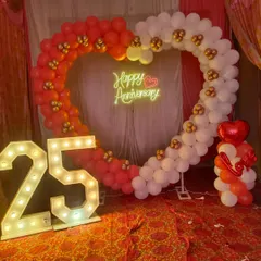 25th anniversary jaise bade function ke liye hum grand decoration karte hain. Ismein red aur white balloons ka heart shape arch, '25' number ke light letters, aur 'Happy Anniversary' ka neon sign shaamil hai.