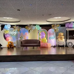 A full view of a spectacular pastel rainbow stage I designed for a large baby shower. The setup features a "Girl or Boy?" reveal sign, a crescent moon prop, multiple backdrops, and a decorative candy cart, all tied together with a vibrant color scheme.