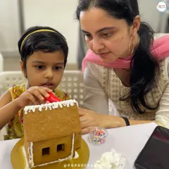 A mother helps her daughter carefully apply icing to the walls of her gingerbread house. It's a perfect parent-child bonding activity.