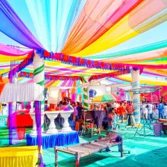 This is a large-scale Holi party pandal I decorated. I used vibrant, multi-colored fabric drapes across the ceiling and arranged traditional charpai seating to create a lively and authentic desi celebration space for the community.
