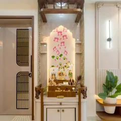 A close-up of a custom mandir with a beautiful lotus-themed backlit panel. The wooden frame and white storage cabinet create a clean and elegant look, perfect for a modern home.
