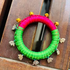A close-up of the kids' bangle. It's a wooden base wrapped in bright pink and green satin thread, with little elephant charms and ghungroos that jingle.