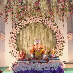 This large-scale decoration features a beautiful circular arch and a ceiling adorned with hanging pink flowers. It’s a design that fills the space with elegance and is perfect for larger idols and society pandals.