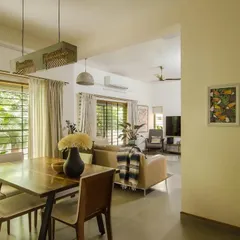 The dining area is now seamlessly connected to the living room, with large windows that look out onto the lush garden. The simple wooden dining table is complemented by contemporary lighting fixtures.