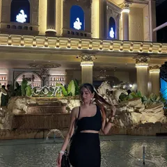 The same black dress, this time in front of a grand, lit-up building. This shows how the outfit works in a more glamorous, upscale setting.