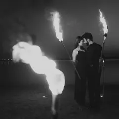 A striking black and white image of a couple surrounded by fire torches at dusk. The high contrast between the flames and the darkness creates a powerful, timeless photograph.
