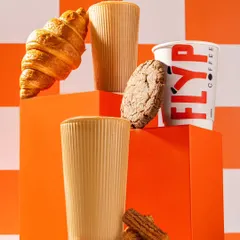 A styled product shoot for Flyp Coffee, featuring their coffee and baked goods. The use of geometric blocks and a bold orange color palette creates a modern and energetic brand look.