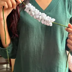 This photo shows the full length of the crochet gajra with its green tie-strings. It's long enough to be styled in many different ways, whether in a bun or a braid.