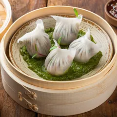Steamed dim sum in a traditional bamboo basket. The styling focuses on the delicate folds of the dumplings and the fresh green pesto sauce, creating an authentic image.