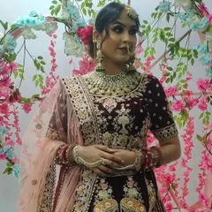 This bride is wearing a deep maroon velvet lehenga with silver floral embroidery, paired with a stunning emerald green jewellery set for a beautiful contrast.