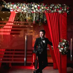 A stylish portrait of the groom at his engagement party. He leans against a doorway framed by red curtains, creating a cool and confident look that is both modern and classic.