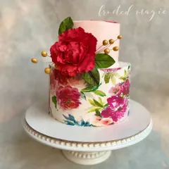 This two-tiered cake combines modern elegance with artistry. The bottom tier is wrapped in a printed floral design, complemented by a large, handmade red sugar peony that adds a touch of drama.
