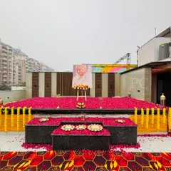 An open-air terrace setup for a Guruji satsang. The stage area is covered in a bed of red rose petals and bordered with marigold garlands, creating a vibrant and sacred space.