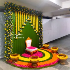 This puberty function decoration combines a vibrant floral rangoli with a traditional marigold backdrop. The setup is completed with a special chair for the ceremony and brass urlis filled with flowers.