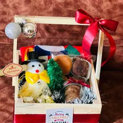 A charming Christmas hamper in a wooden basket. This gift includes a snowman figurine, a miniature Christmas tree, cookies, and other festive treats.