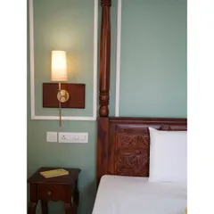 A close-up of the master bedroom in the Raghuvani Home, showing the intricate carving on the Sheesham wood four-poster bed and the elegant wall-mounted sconce, creating a perfect blend of traditional craftsmanship and modern lighting.