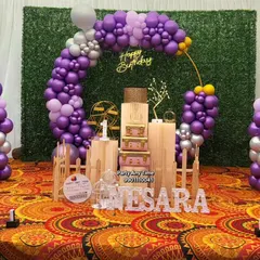A full view of Nesara's first birthday decoration with a purple and silver color scheme. The setup includes a picket fence and vintage-style props.