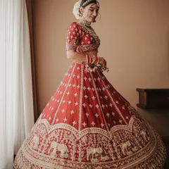 A full-length portrait showcasing the magnificent twirl of the bride's red lehenga. The intricate elephant motifs and her joyful expression are beautifully captured against a clean, bright background.