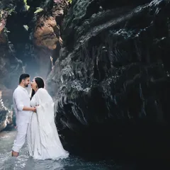 A serene pre-wedding shoot in a natural cave. The couple, dressed in white, stands in the water, creating a beautiful contrast with the dark, textured rocks for a truly epic portrait.