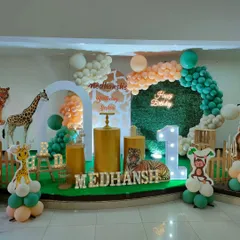 A modern safari theme using gold pedestals and a clean, arched backdrop against a grass wall. A neon sign and marquee letters add a bright, celebratory touch.