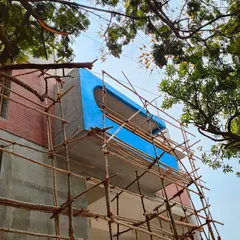 'Project 83' standing tall during construction, wrapped in traditional bamboo scaffolding. This photo captures the building taking shape, showcasing the bold blue balcony feature against the raw concrete and brick structure.