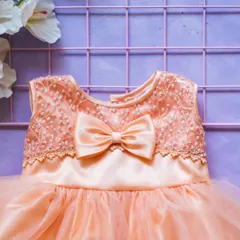 This peach-colored dress features a bodice with intricate floral embroidery and a delicate lace trim. A satin bow completes this sweet and sophisticated design.