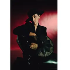 A portrait from the 'Levels of Power' series, featuring a model in a black hat and suit against a smoky red background. The dramatic lighting and commanding pose evoke a sense of authority and mystery.