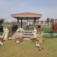 A charming and rustic entrance decor for a daytime garden event. The setup includes floral arrangements in wicker baskets, lanterns, and elegant statues flanking the steps of a gazebo.