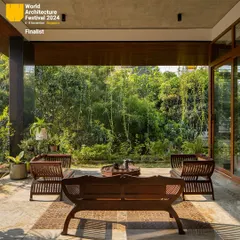 A quiet outdoor seating area designed for relaxation and conversation. The space is sheltered by the building's overhang while remaining completely open to the garden, offering a perfect example of indoor-outdoor living.