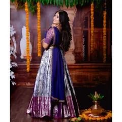 A back view of the purple half-saree, showcasing the full lehenga skirt and the traditional backdrop decorated with marigolds.