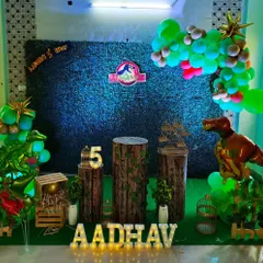 A Jurassic Park inspired dinosaur theme with a dark grass wall and wood-textured pedestals. Foil dinosaur balloons and marquee letters add to the prehistoric vibe.