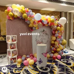 A "Baby in Bloom" themed baby shower backdrop with a colorful balloon arch and transparent "BABY" blocks.