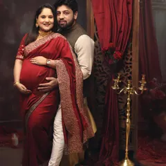 This portrait captures the rich color and texture of a traditional red saree. The couple poses against a backdrop of red drapes and a candelabra, creating a warm and opulent feel.