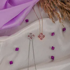 Close-up product shot of clover-shaped necklaces in silver and rose gold. The soft, draped fabric background adds a touch of luxury and helps the metallic details stand out.