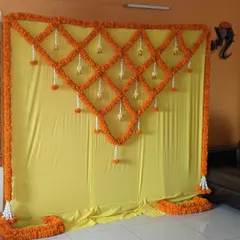 A beautiful and simple backdrop made entirely of fresh marigold flowers. The geometric lattice pattern with hanging bells is a traditional and fragrant choice for an at home Haldi or Pooja ceremony.