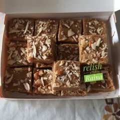 A box of Gur Padi or Sukhdi, a classic Gujarati sweet. Made with whole wheat flour, pure ghee, and jaggery, it has a delightful crispy texture and is topped with sliced almonds.